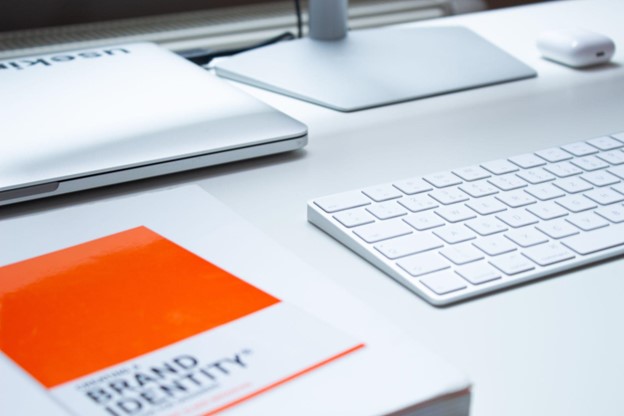 photo of work space with brand identity book, keyboard, and laptop on desk 